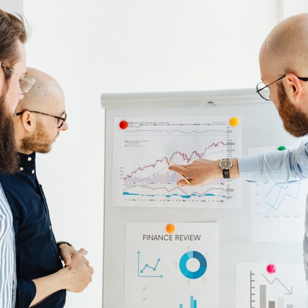 3 men are analyzing financial reports on a chart