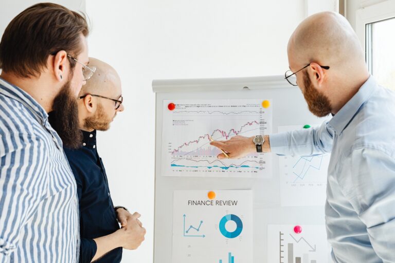 3 men are analyzing financial reports on a chart