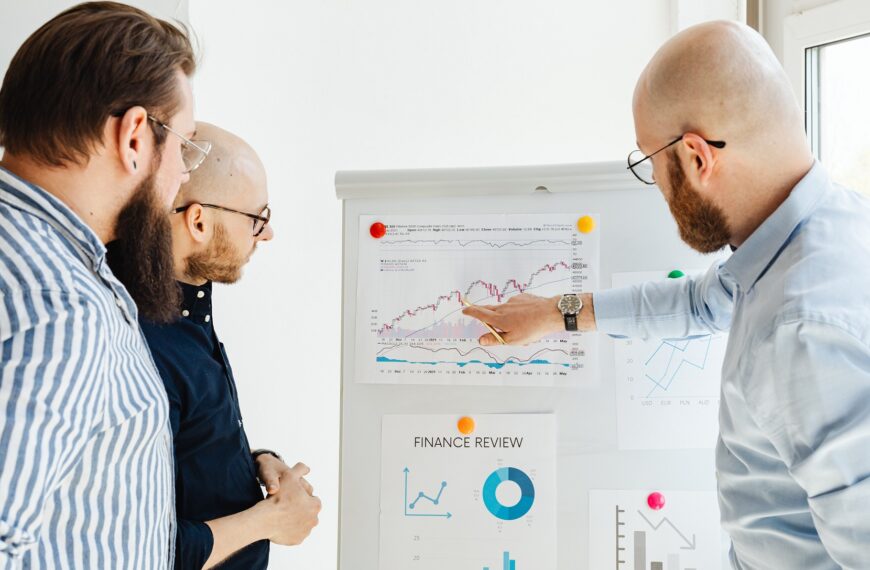 3 men are analyzing financial reports on a chart