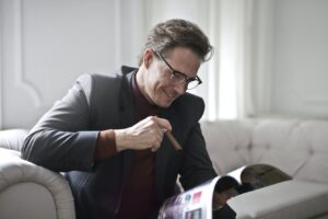 A man sitting on a couch with a cigar while reading a magazine