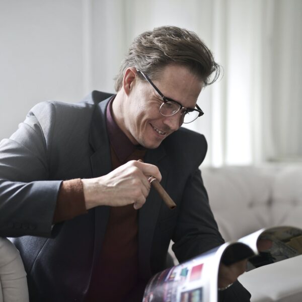 A man sitting on a couch with a cigar while reading a magazine