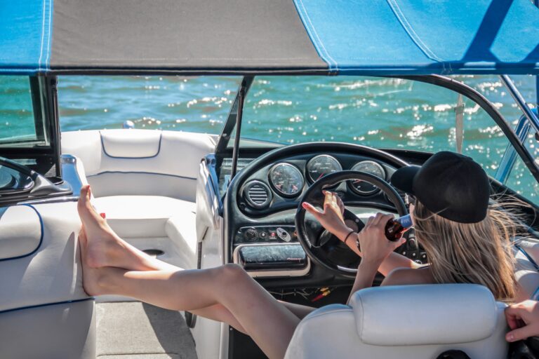 Woman sits in the driver seat of a boat as she relaxes with a drink in hand.