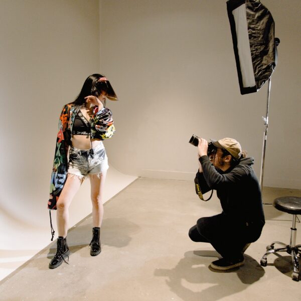 A fashion photo shoot with a young woman posing for the camera while the photographer bends down to get the perfect shot.