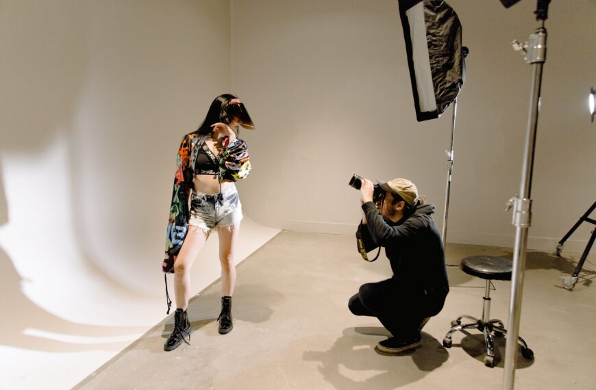 A fashion photo shoot with a young woman posing for the camera while the photographer bends down to get the perfect shot.