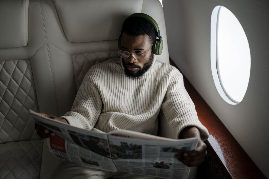 A man sits in a private jet reading a newspaper.